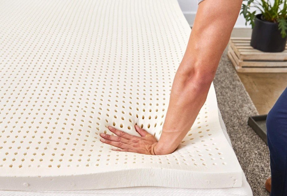 Hand pressing into a Neonap natural latex mattress, showing the perforated latex surface